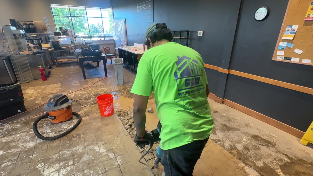 Worker using jackhammer to break concrete during demolition